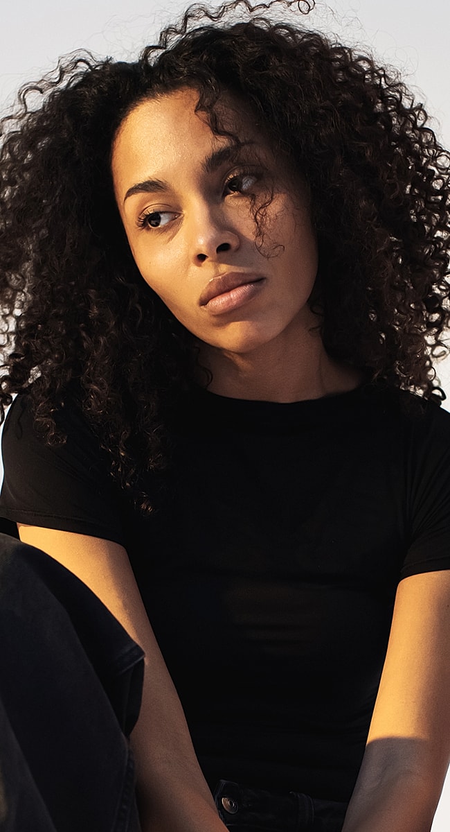Young woman with curly hair, thoughtful expression.