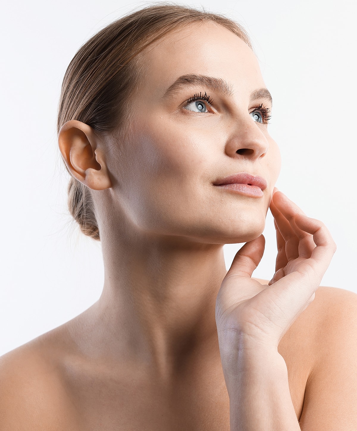 Woman softly touching her face, looking upward.