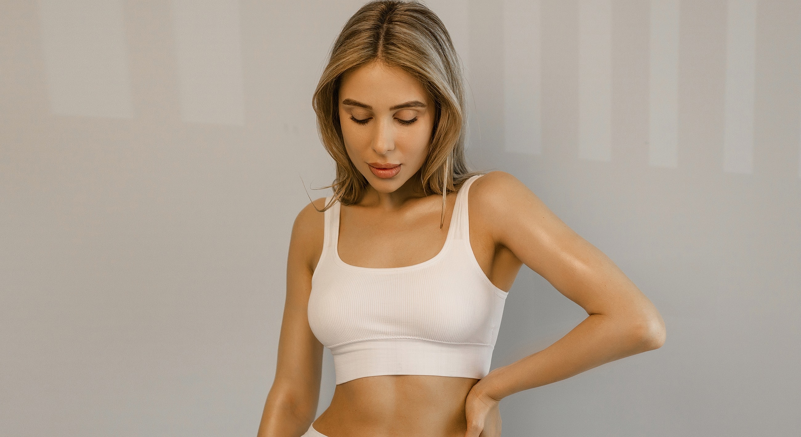 Charlotte, NC breast reduction and lift model in white crop top looking down.